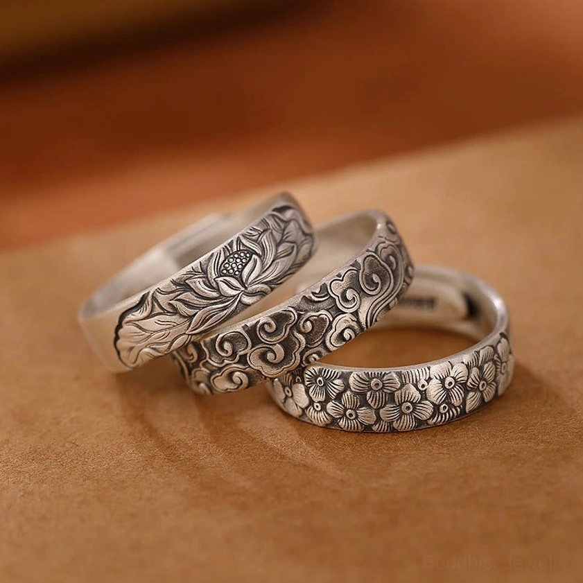Three handcrafted 999 sterling silver Buddhist rings with engraved lotus, plum blossom, and auspicious cloud designs displayed on brown leather, top-down flat lay view
