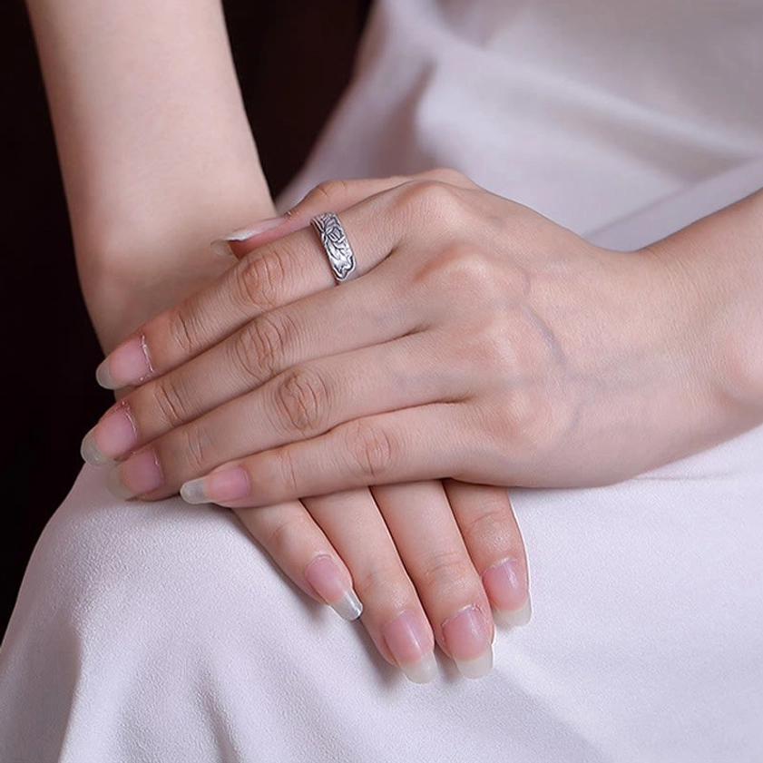 Woman wearing delicate floral engraved sterling silver Buddhist ring on finger, side view with white dress showing ring in natural wear