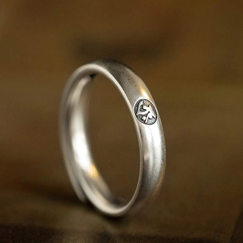 Single sterling silver zodiac ring with embossed Buddhist natal buddha mark, three-quarter front view on wooden surface
