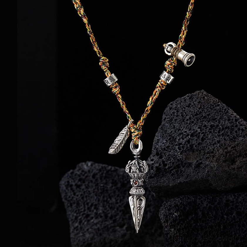 Close-up Detail of Five-Pronged Dorje Pendant with Silver Feather Charm and Multicolored Woven Rope Necklace Against Volcanic Stone Background