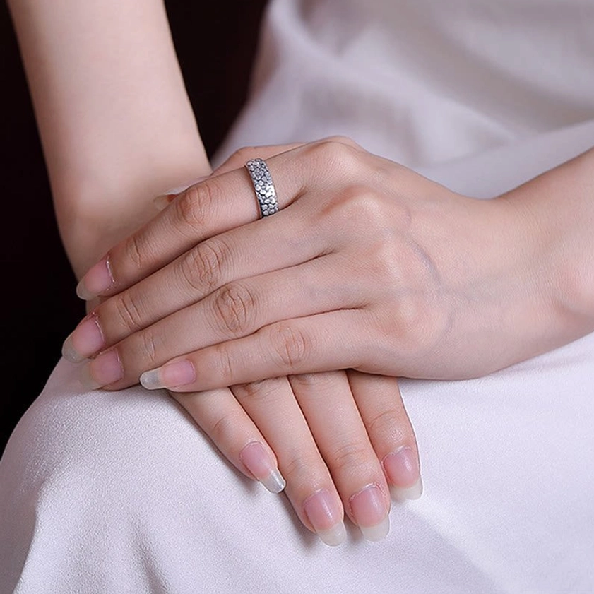 Woman wearing delicate tiny clustered flower engraved sterling silver Buddhist ring on finger, side view with white dress showing spiritual jewelry in daily wear