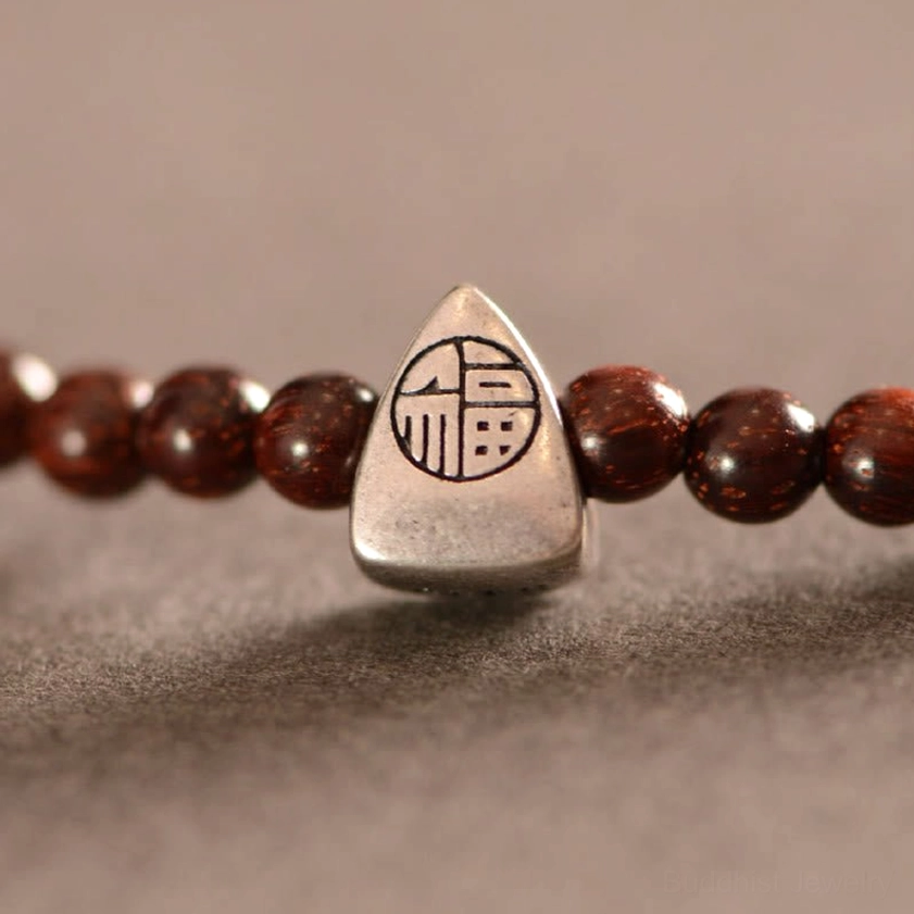 Macro detail of engraved 925 sterling silver Fu character charm pendant with polished sandalwood beads