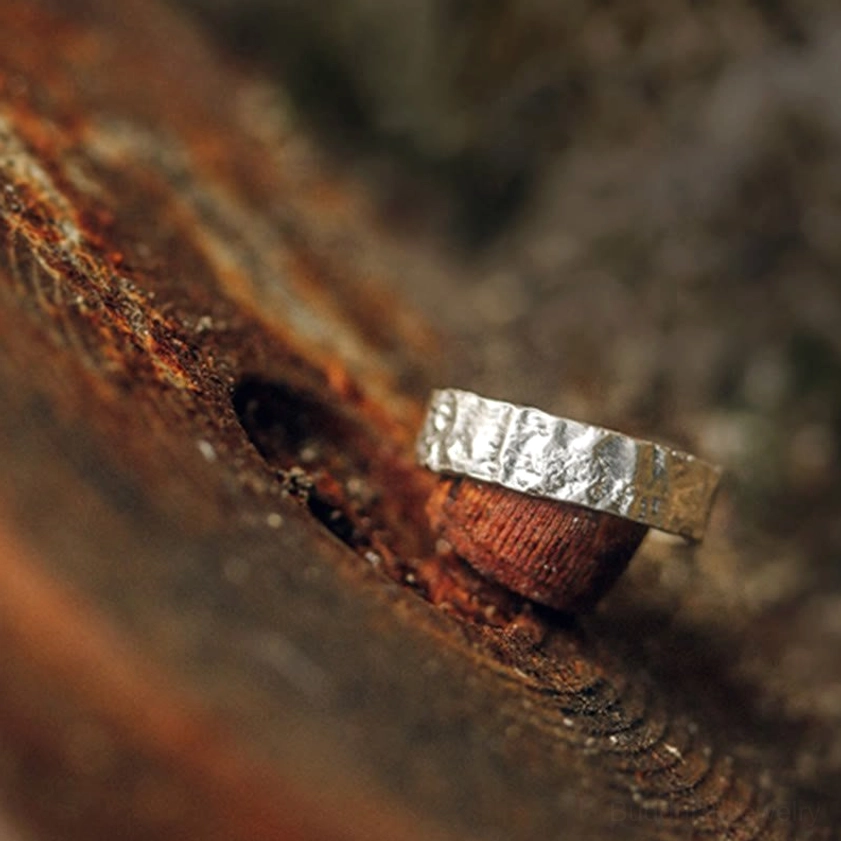 Single silver hammered textured band ring, oblique angle on rustic wooden surface