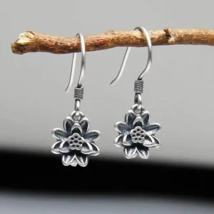 Sterling silver lotus flower dangle earrings with 3D carved lotus petals and antique silver finish, displayed on wooden branch