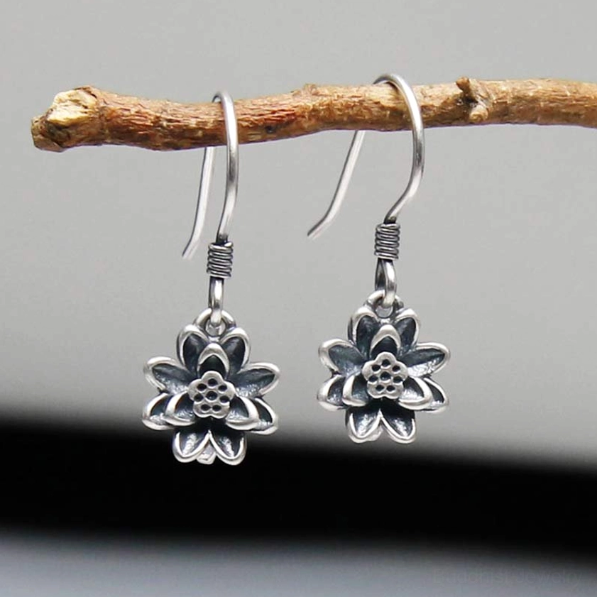 Sterling silver lotus flower dangle earrings with 3D carved lotus petals and antique silver finish, displayed on wooden branch
