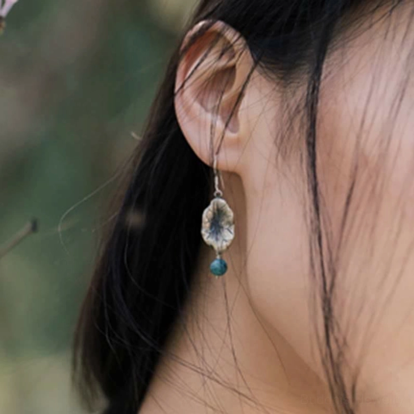 Silver lotus leaf dangle earrings side view worn on ear in floral garden setting
