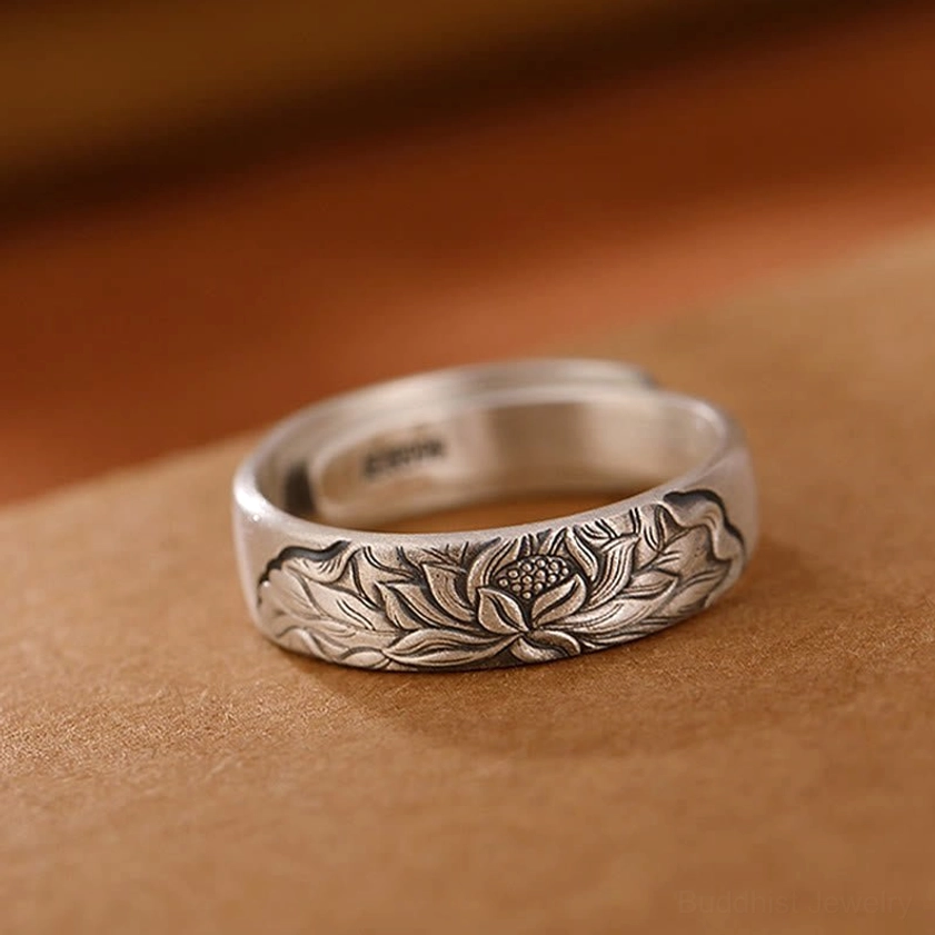 Lotus flower patterned sterling silver adjustable open ring top-down side view on light brown leather displaying full engraved lotus details