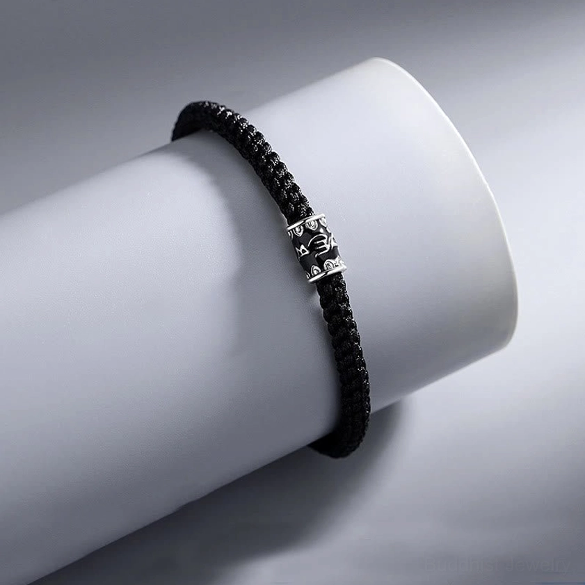 Buddhist prayer string bracelet side view on display showing black braided cord and vintage silver accent bead