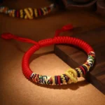 925 Sterling Silver Om Mani Padme Hum King Kong Knot bracelet with red rope and golden knot detail on wooden desktop
