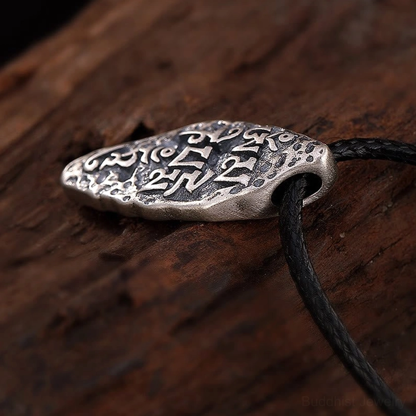 925 sterling silver Om Mani Padme Hum pendant attached to black leather cord, back oblique angle on dark wooden surface
