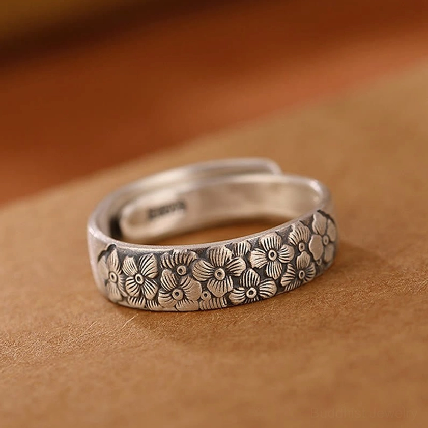 Plum blossom sterling silver adjustable open ring top-down side view on light brown leather showing full clustered flower engravings and adjustable band design
