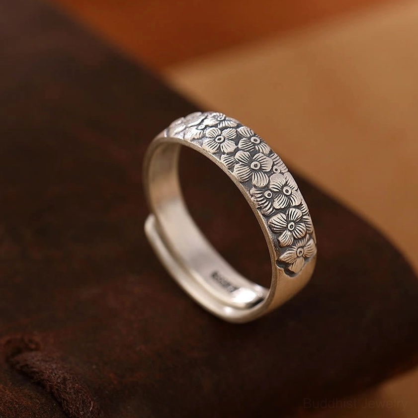 Plum blossom engraved sterling silver adjustable ring three-quarter view on dark brown leather displaying clustered floral pattern and antique silver tone
