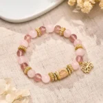 Strawberry rose quartz Buddhist bracelet with gold lotus charm displayed on linen fabric and dried florals