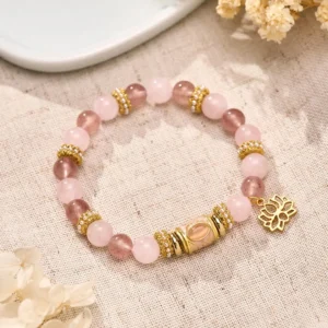 Strawberry rose quartz Buddhist bracelet with gold lotus charm displayed on linen fabric and dried florals