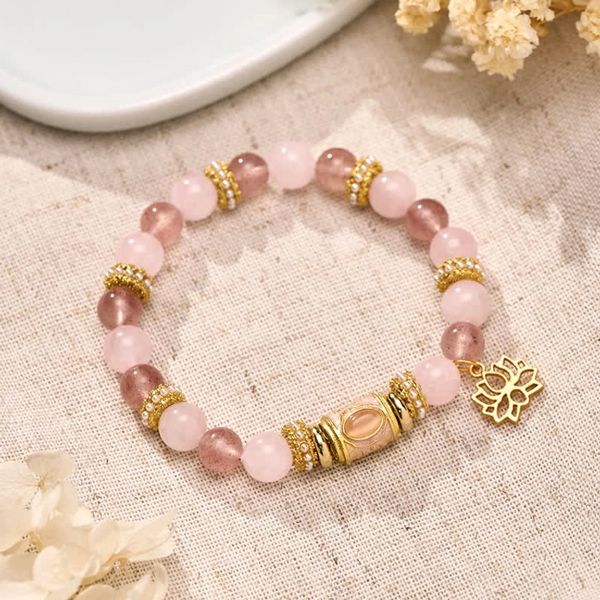 Strawberry rose quartz Buddhist bracelet with gold lotus charm displayed on linen fabric and dried florals