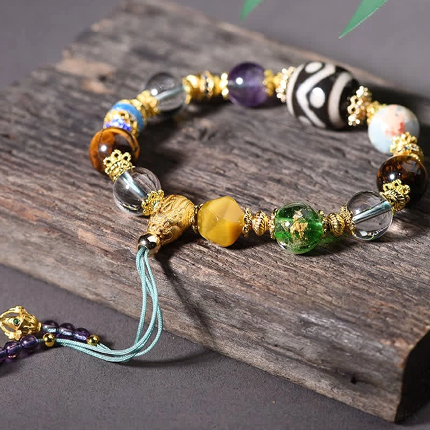 Stretched Buddhist bracelet with mixed gemstones displaying individual Dzi bead, amethyst, and tiger eye beads on wood