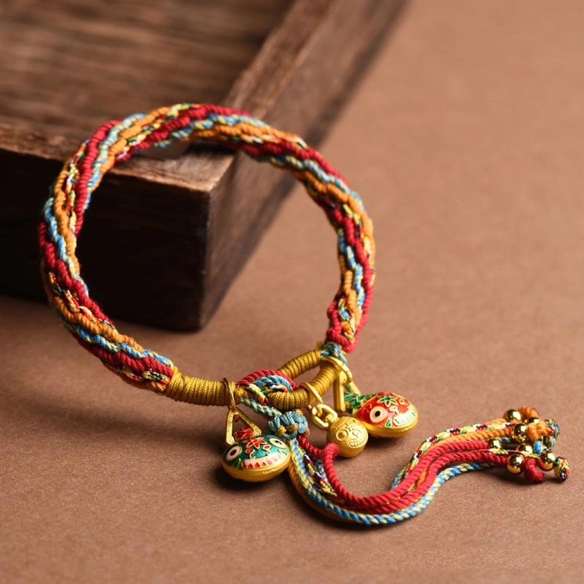 Folk style braided rope bracelet with gold enamel beast pendants and tassel detail, side close-up on wooden box background