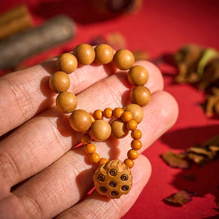 Tan sandalwood meditation palm beads with carved lotus pod charm in hand-held first-person close-up, showing warm brown wooden beads and orange spacer accents
