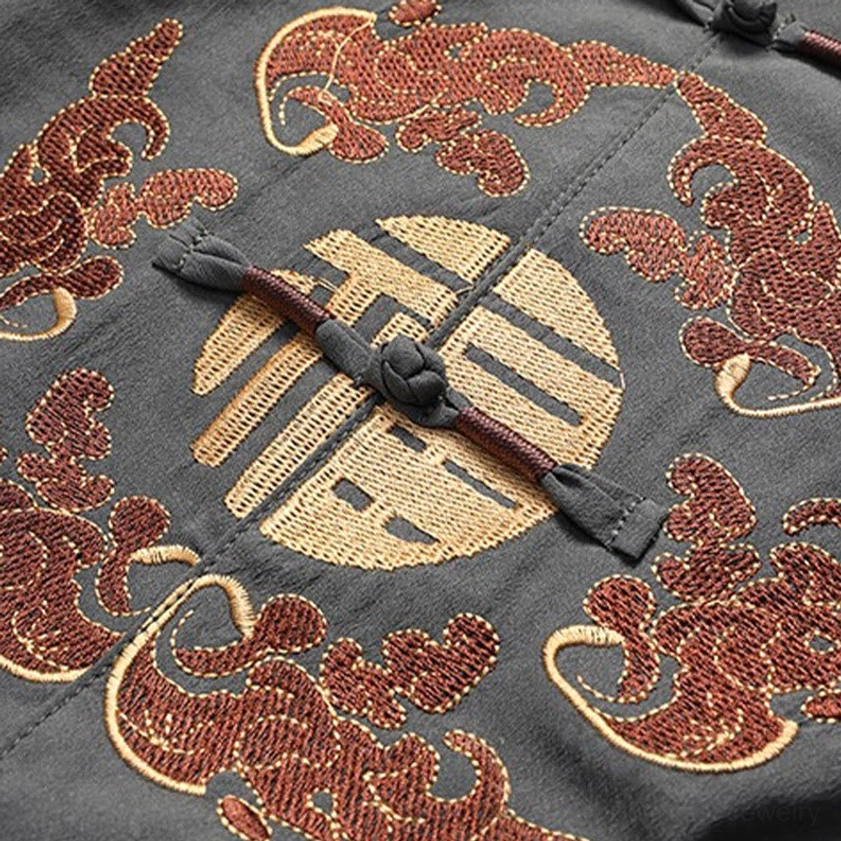 Embroidered Fu character and lucky bat pattern with gold accents on dark Tang suit fabric, close-up of auspicious design element