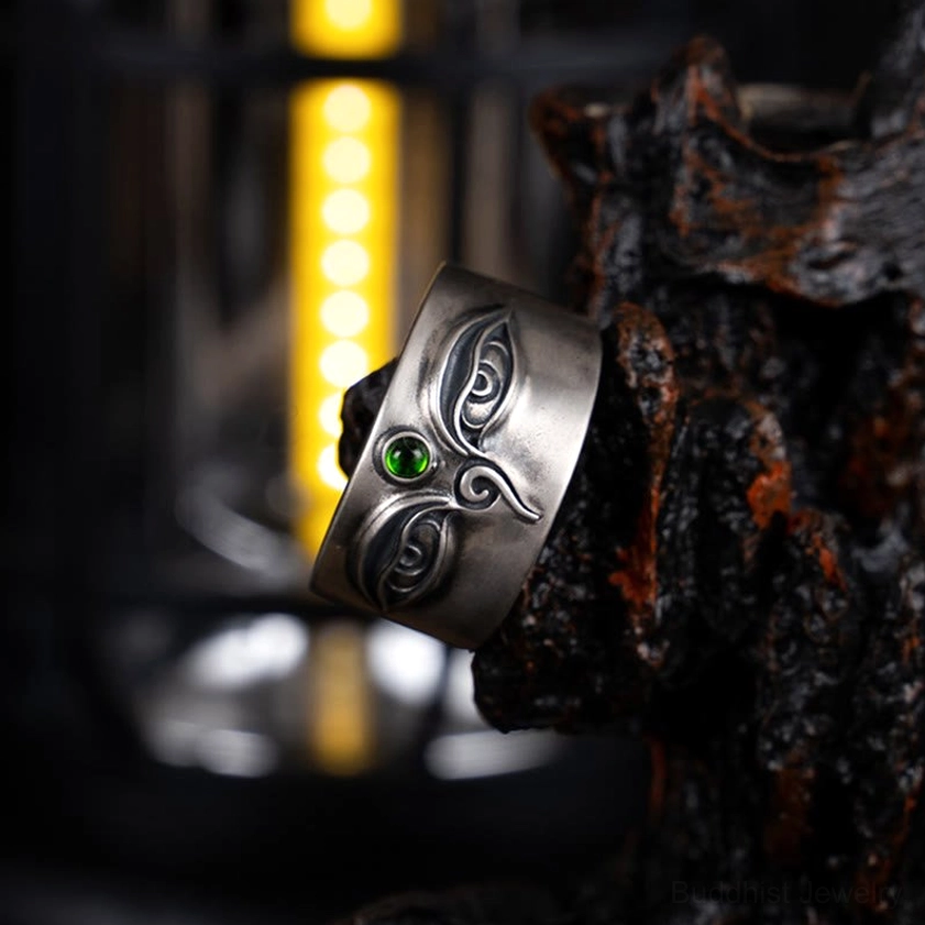 Low angle side view of 925 sterling silver Tara adjustable ring with antique finish, eye engraving, and green gemstone inlay under warm backlighting