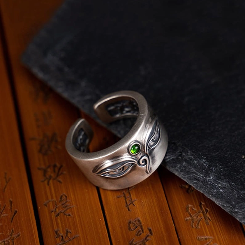 Side oblique view of handmade Tara protection ring in antique sterling silver with eye carving and green gemstone on Chinese calligraphy wooden board