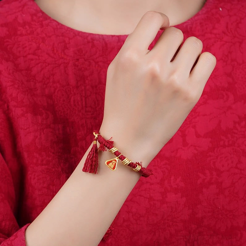 Red tassel bracelet worn on wrist showing proper fit and placement, photographed from side angle with red fabric background