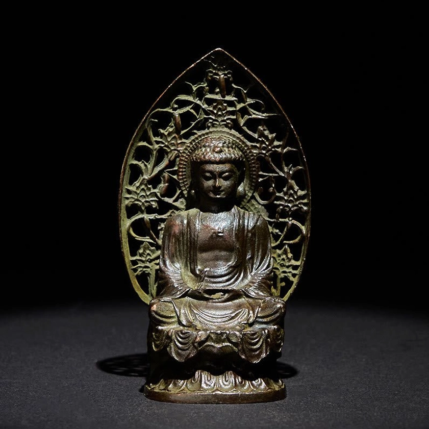 Tathagata Buddha alloy statue frontal view with antique bronze patina and hollowed floral backboard on dark background