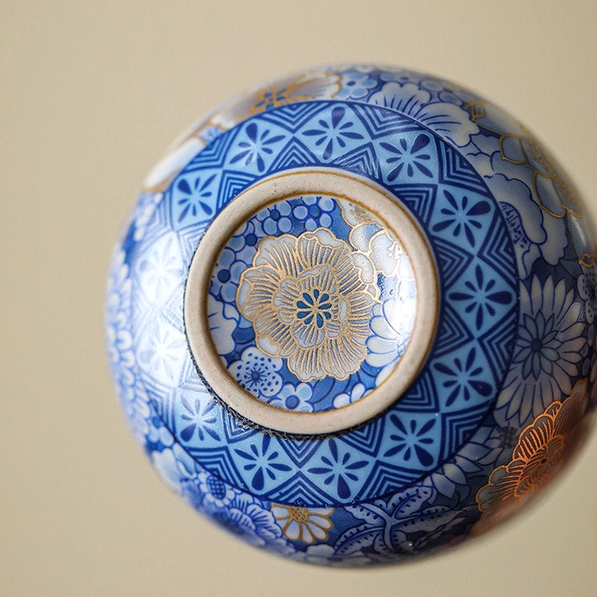 Bottom detail of porcelain tea cup showing geometric blue border and central gold floral pattern