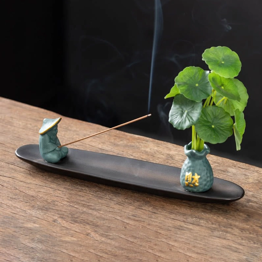 Teal blue Fisherman Buddhist incense holder set with figurine, vase, and burning incense stick on dark wooden surface