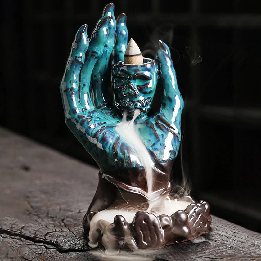Teal blue glazed ceramic skull hand incense burner with lotus-shaped base and flowing smoke