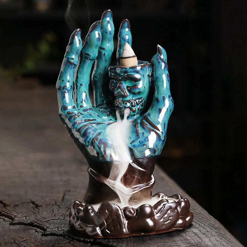 Two-tone teal and brown ceramic skull hand incense burner with active smoke waterfall effect