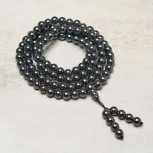 108 bead Terahertz mala prayer beads coiled on light neutral surface, dark metallic polished beads with tassel pendant