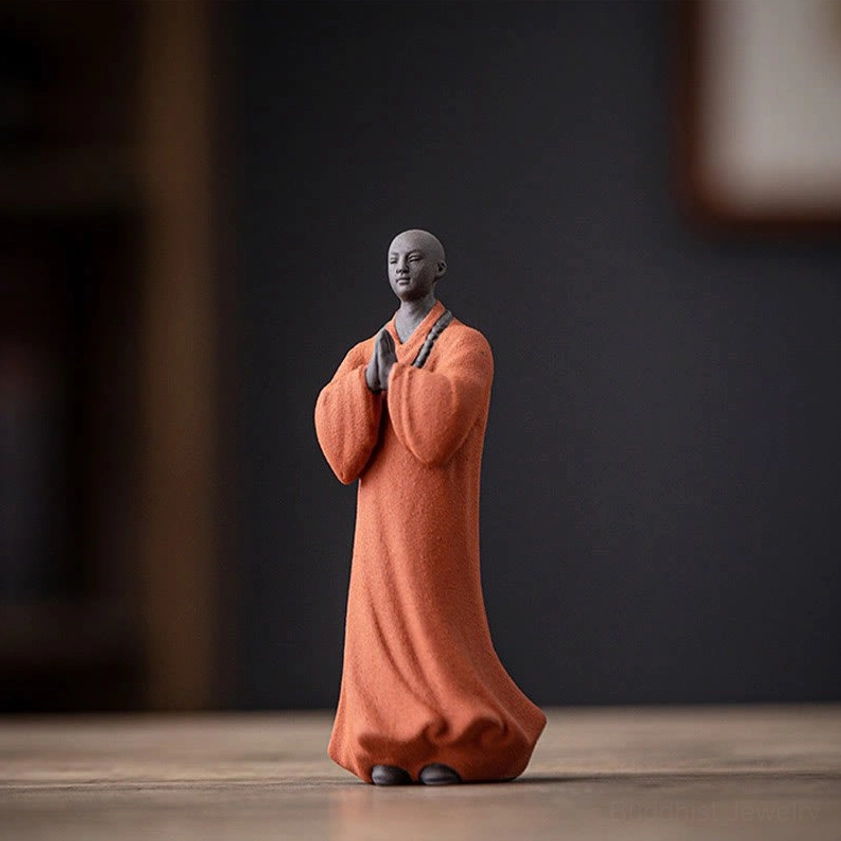 Single terracotta orange ceramic meditation monk statue with smooth dark head and matte robe texture