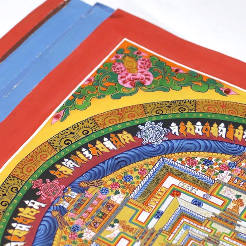 Close-up detail of stacked handmade Thangka canvas edges showing red and blue fabric borders and intricate decorative patterns