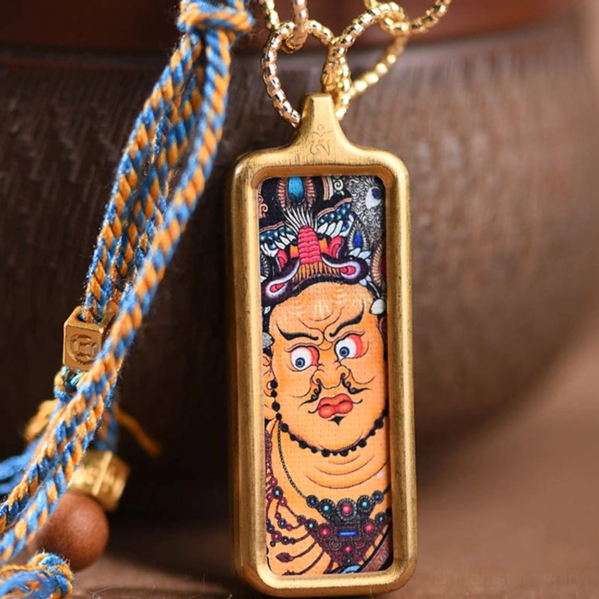 Close-up of wrathful wealth deity thangka pendant with blue and yellow braided cord and gold metal frame detail