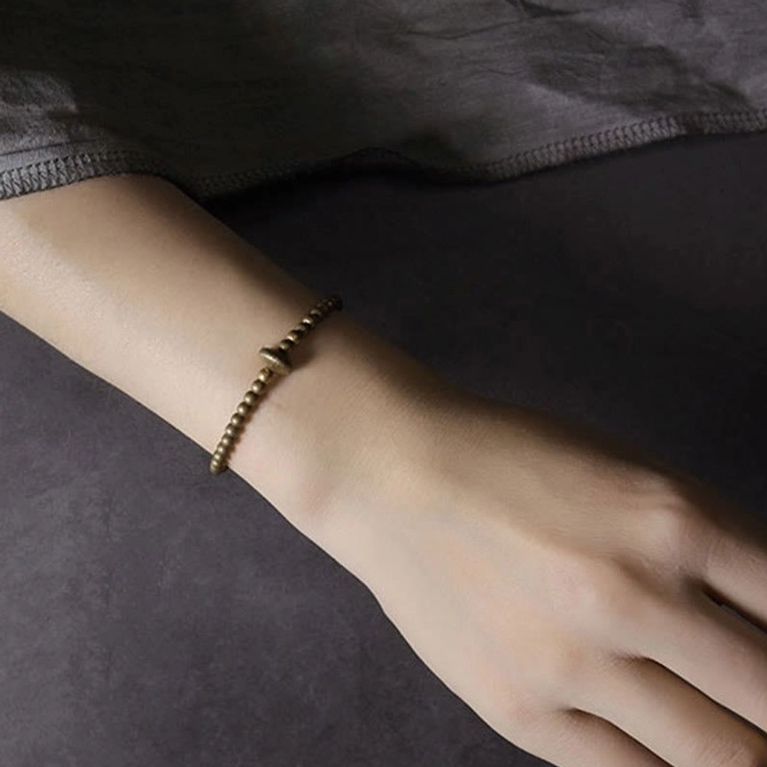 Slim minimalist copper bracelet on wrist with antiqued brass finish against neutral background