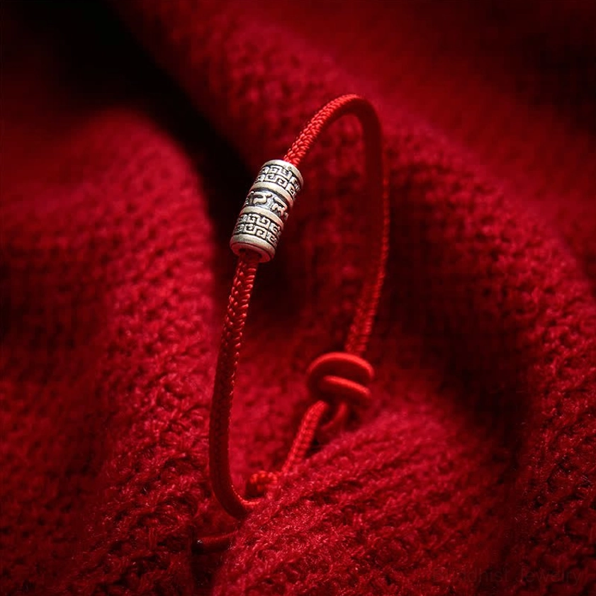Thin red string Buddhist bracelet with engraved silver bead and adjustable sliding knot, close-up macro view