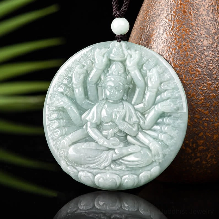 Thousand-hand Guanyin jade pendant flat display with decorative pottery and green foliage background, detailed relief carving in light cyan jade with reflection