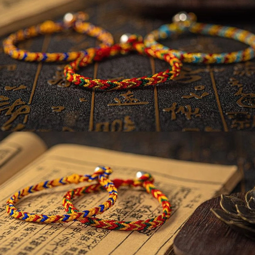 Three handcrafted multicolored Buddhist string bracelets arranged overhead with uniform braided pattern on dark background with golden sacred characters