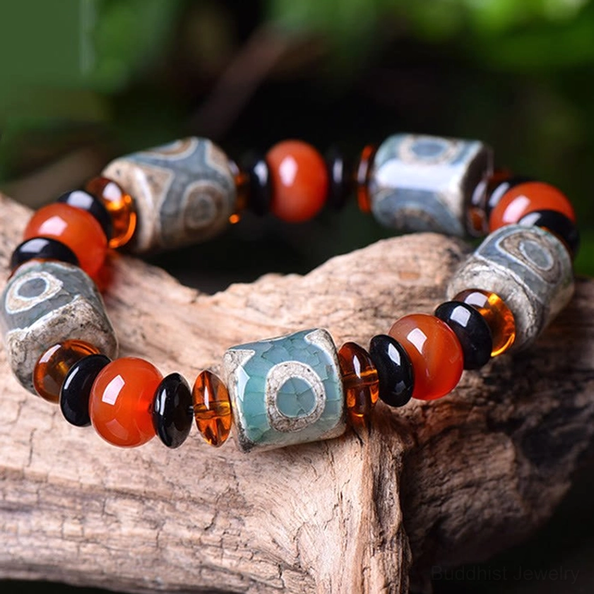 Three-eye Dzi agate bracelet close-up angled view on light wooden background, showing detailed bead pattern and glass separator beads