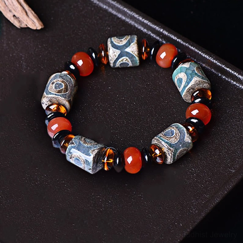 Three-eye Dzi bead agate bracelet overhead flat lay on black display tray, circular arrangement showing full protective amulet design