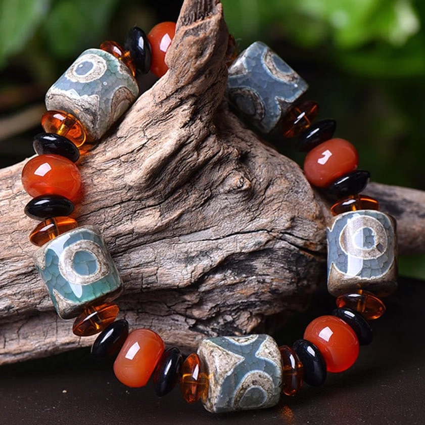 Three-eye Dzi bead Buddhist bracelet side view draped on weathered driftwood, displaying carnelian spacers and protective amulet design