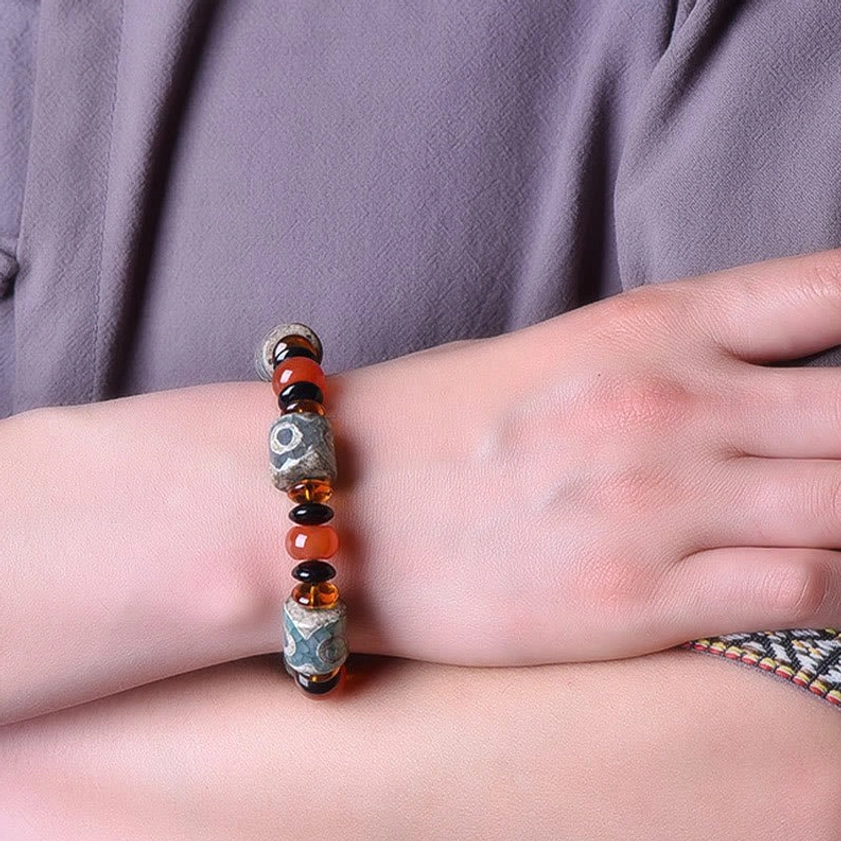 Three-eye Dzi bead bracelet worn on wrist lifestyle photo with grey fabric, demonstrating comfortable fit for Buddhist spiritual practice