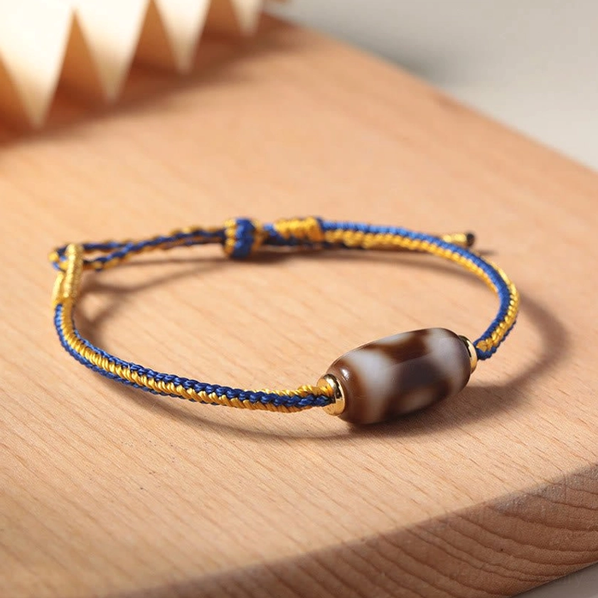 Polished brown and white three-eye Dzi bead bracelet with gold hardware accents on wooden board high angle view