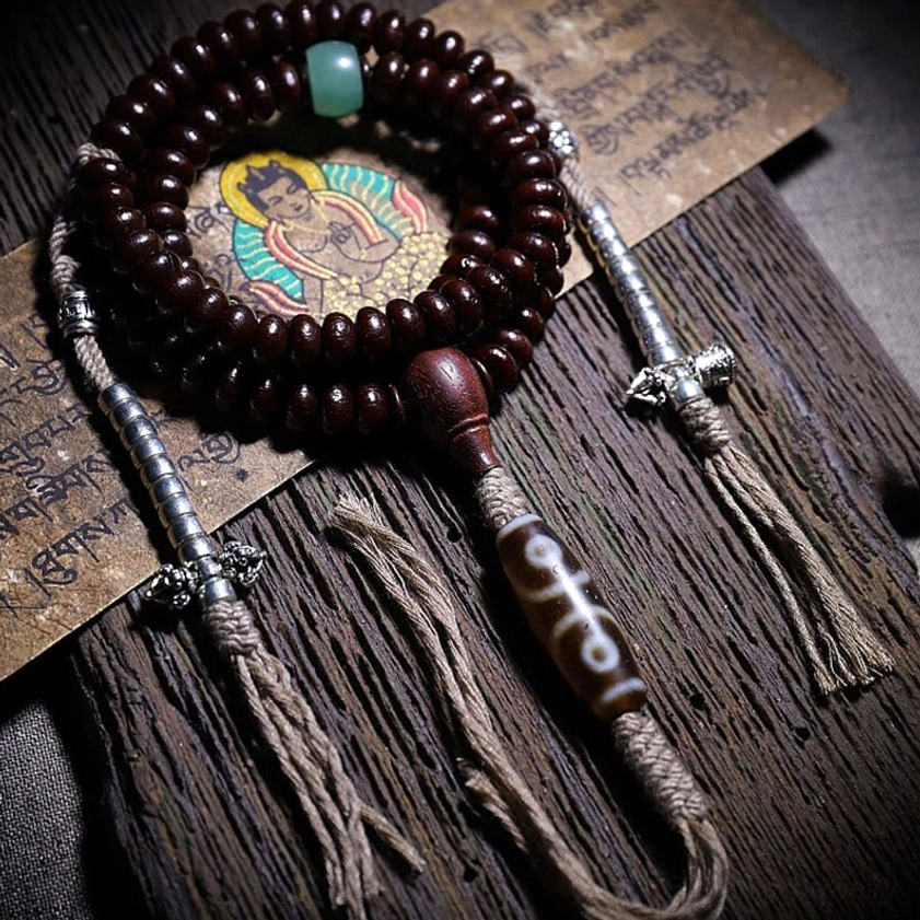 Three-eyed dzi bead mala bracelet with dark bodhi seeds and spiritual dorje charm on wood surface