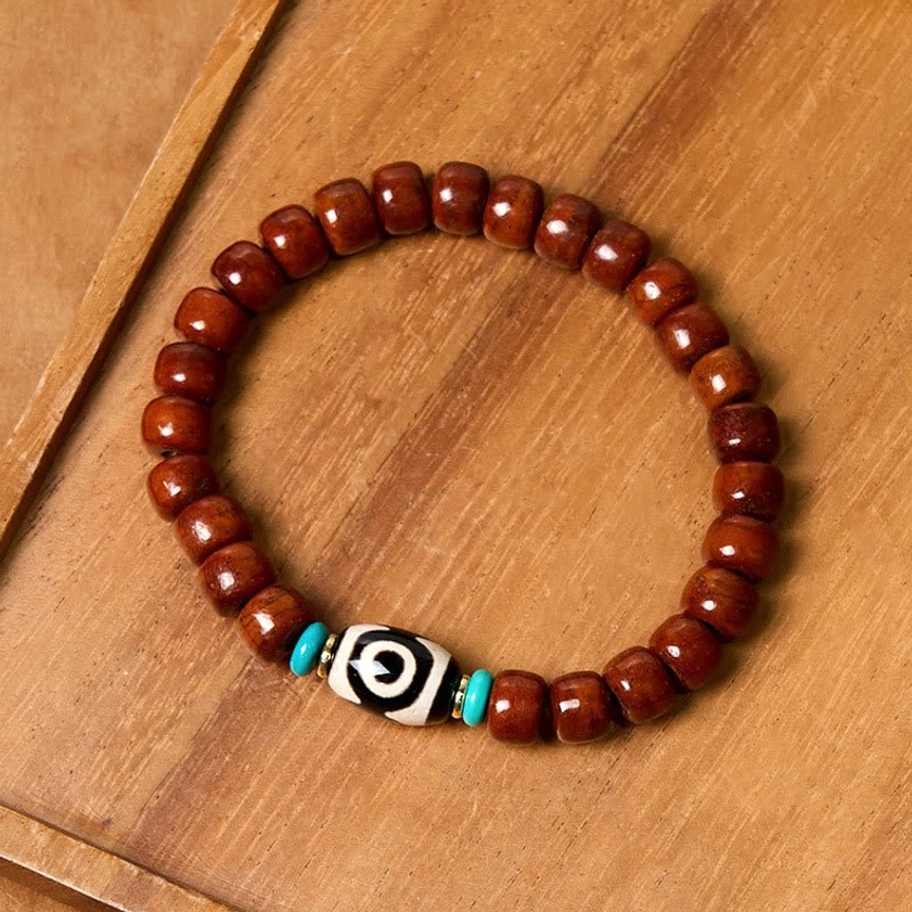 Three-eye Dzi luck bone bead bracelet flat lay top-down view showing full circular bracelet with black-white Dzi bead and turquoise spacers