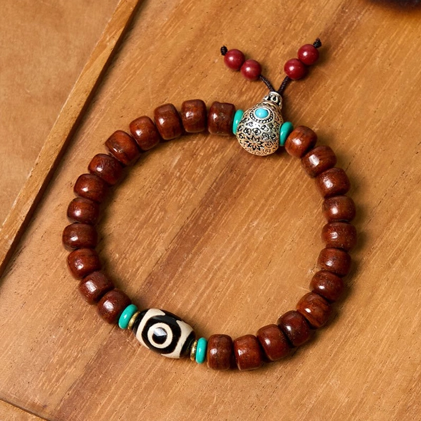 Tibetan three-eye Dzi bracelet flat lay top-down view showing reddish-brown bone beads, silver turquoise inlaid spacers, and red hanging beads