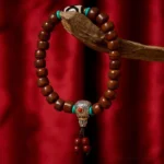 Three-eyed Dzi bone bead bracelet with Tibetan silver clasp and red tassel, side overhead view on wooden prop with red fabric background
