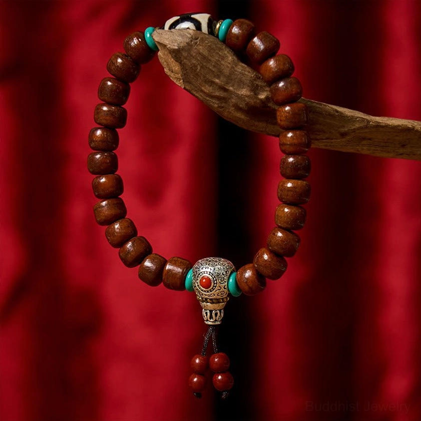 Three-eyed Dzi bone bead bracelet with Tibetan silver clasp and red tassel, side overhead view on wooden prop with red fabric background