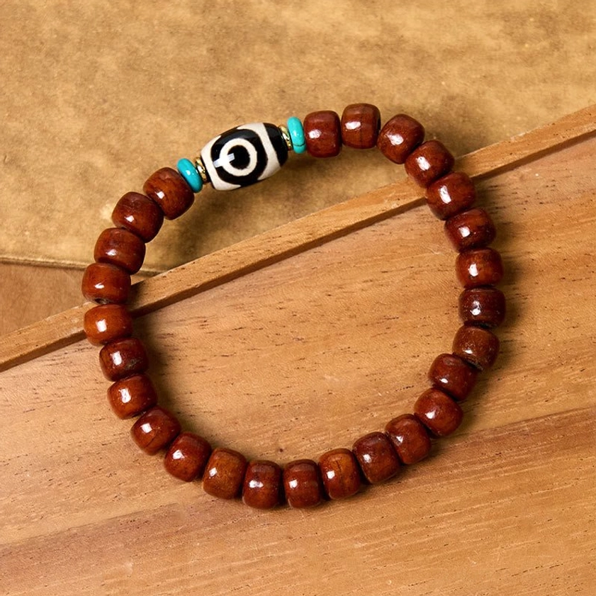 Tibetan Buddhist bone bead bracelet with three-eye Dzi bead worn on wrist showing fit and comfort on wooden background